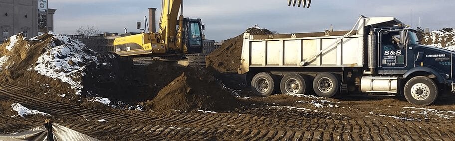 A dump truck and a tractor in the dirt.